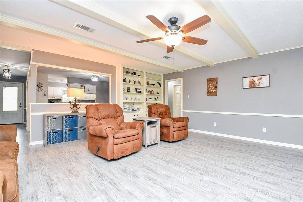 Wow! This is a wide-open-country living space like no other! High, beamed ceiling embraces huge floor/wall space below in this amazing living space, also with built in shelving, a continuation of divine natural tones, with kitchen in the background, up left.