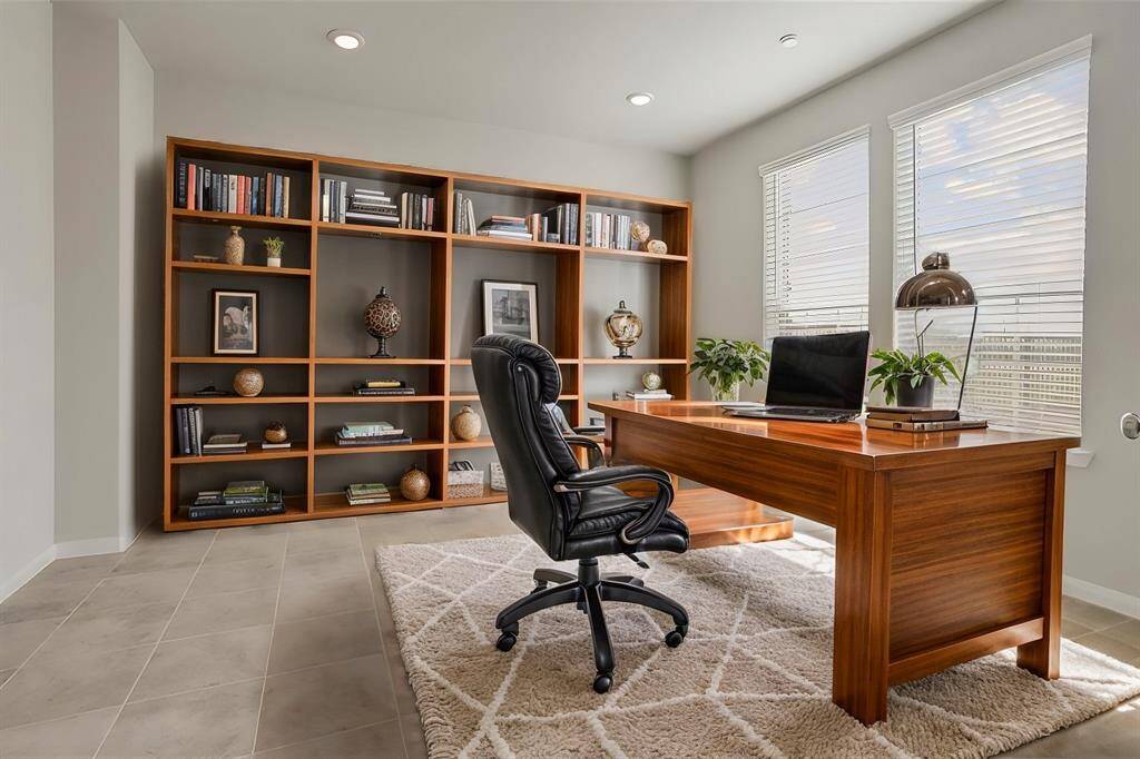 A spacious home office designed for both productivity and comfort, bathed in natural light from a large window fitted with blinds for adjustable brightness and privacy. With ample space for a desk, shelving, and seating, this office is the perfect blend of function and style, creating an inviting workspace within the home. ***Virtually Staged