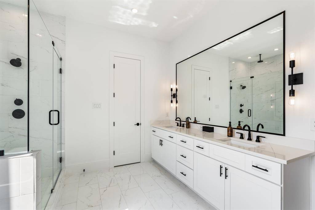 A modern double vanity with quartz countertops and ample storage, complete with stylish black fixtures. The oversized mirror reflects natural light, enhancing the bright and airy ambiance.