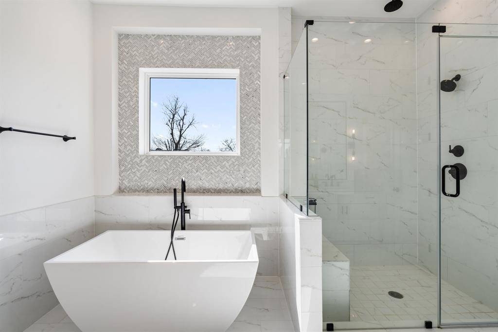 A detailed view of the freestanding soaking tub paired with a rainfall shower behind a glass enclosure. The textured tile accent wall adds depth and elegance to this spa-inspired space.