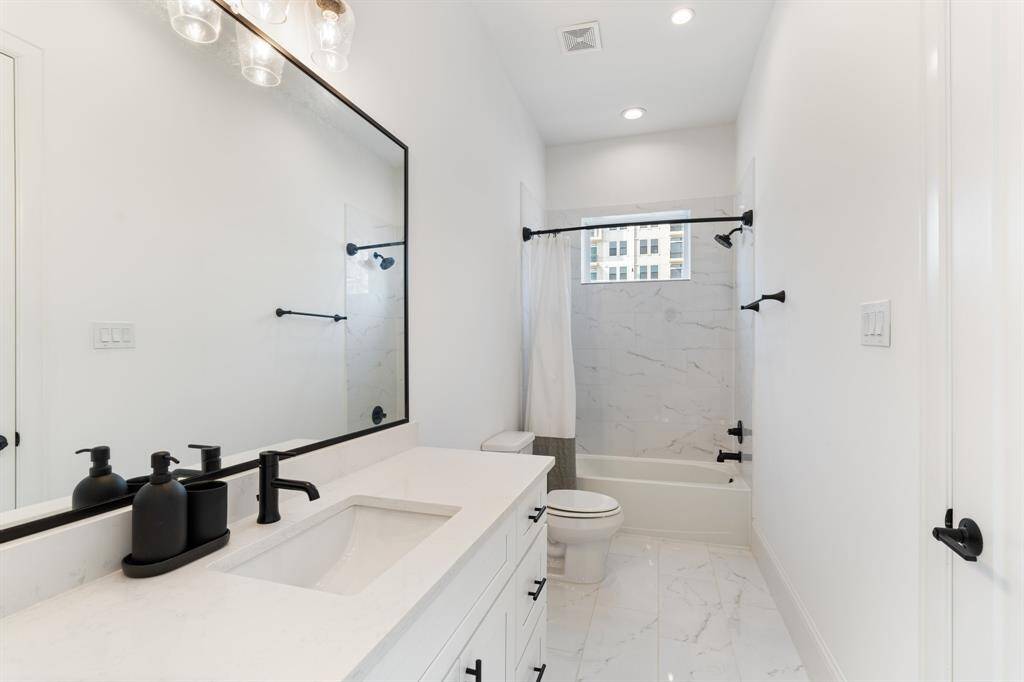 A stylish secondary bathroom with a quartz-topped vanity, modern black fixtures, and sleek tilework in the bath and shower area for a contemporary, polished look.