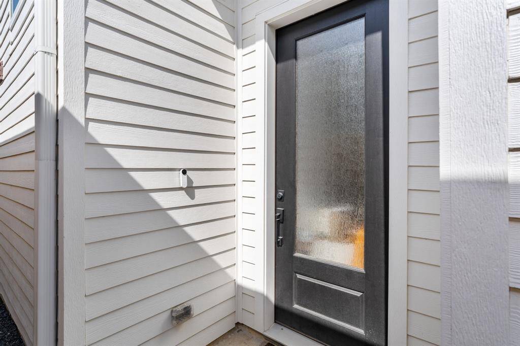 The modern front entry features a sleek glass-paneled door and a smart doorbell for security. The crisp siding and black door create a stylish and welcoming first impression.