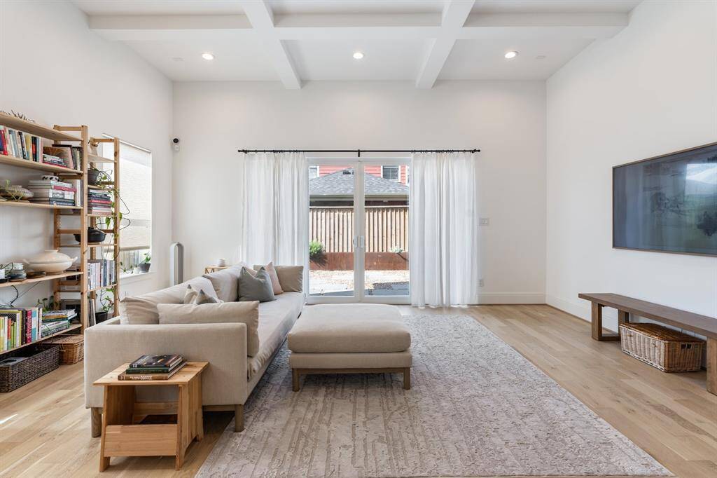 Natural light pours through the expansive patio doors, illuminating the elegant coffered ceilings and crisp white walls. This open and airy space is perfect for both everyday relaxation and entertaining guests.