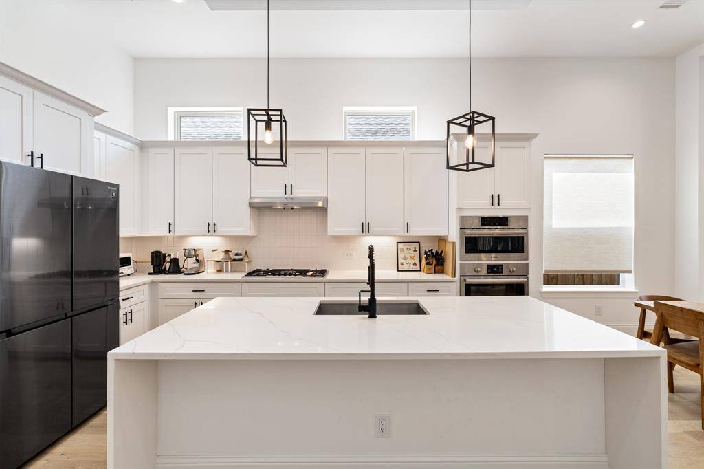 The large quartz island provides generous prep space, complemented by a deep undermount sink and modern matte black fixtures. Stylish pendant lights add a touch of contemporary flair to this culinary haven.