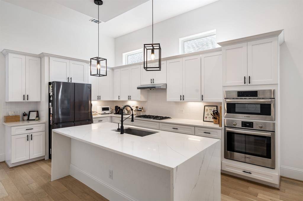 The large quartz island provides generous prep space, complemented by a deep undermount sink and modern matte black fixtures. Stylish pendant lights add a touch of contemporary flair to this culinary haven.