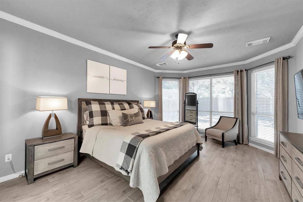 Primary bedroom featuring a seating area, crown molding, engineered wood floors, designer paint and ceiling fan
