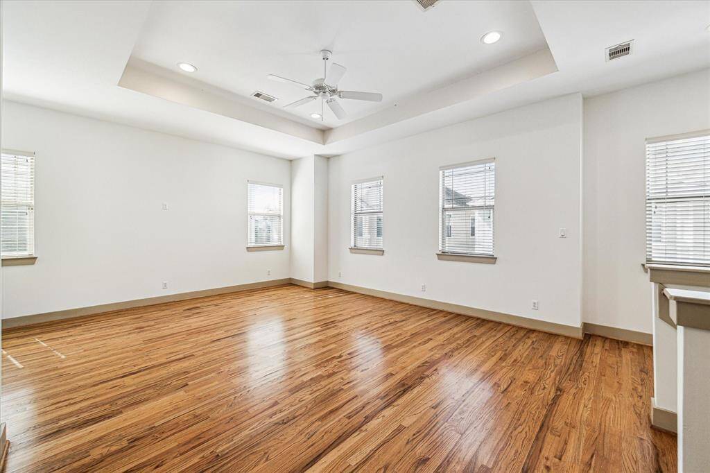LIVING ROOM VIEW  - This spacious room features beautiful hardwood floors, a tray ceiling with recessed lighting, and ample natural light from multiple windows. The neutral color palette provides a versatile backdrop for any décor style.