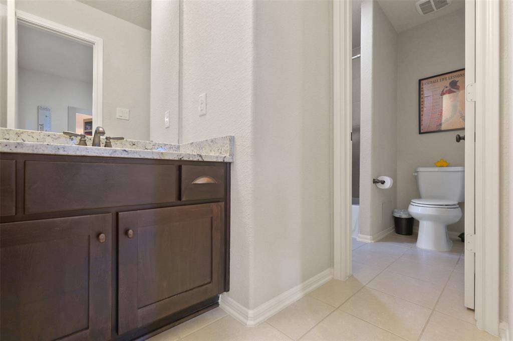 This photo shows a bathroom with a granite countertop and dark wood vanity. The toilet is in a separate alcove, and the flooring is light tile.