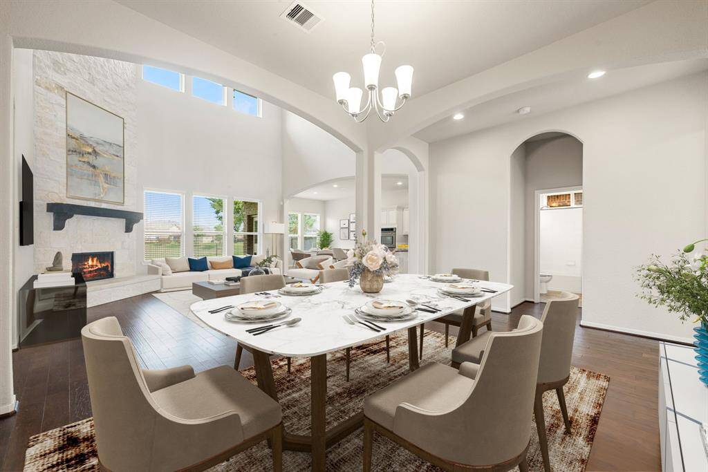 Step into this beautifully designed space featuring soaring ceilings, expansive windows that flood the area with natural light, and a cozy stone fireplace as the centerpiece. The open layout seamlessly connects the living and dining areas, offering an ideal setting for both relaxing and entertaining. Elegant archways and warm wood floors enhance the home's inviting atmosphere, while the spacious design provides ample room to make it your own.