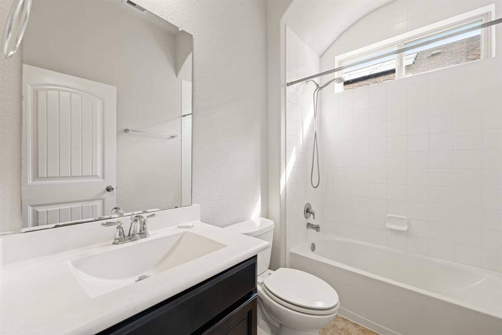 Secondary bath features tile flooring, bath/shower combo with tile surround, dark wood cabinets, beautiful light countertops, mirror, sleek fixtures and modern finishes.