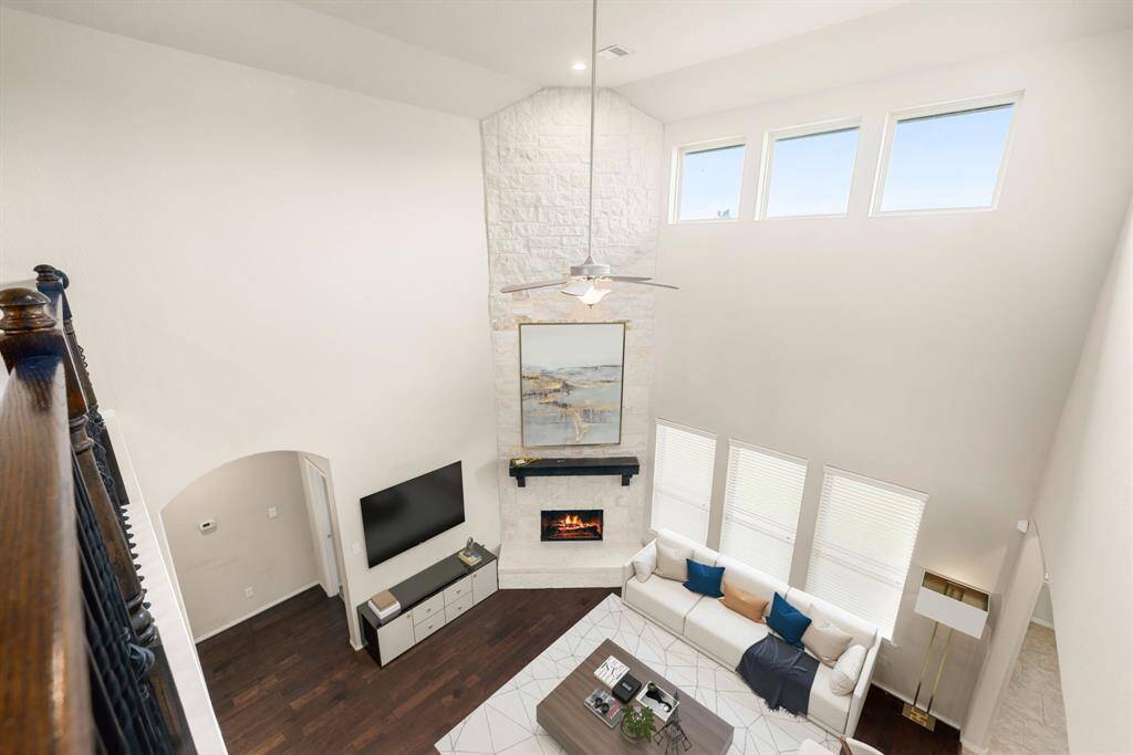 Enjoy the breathtaking view of this elegant living space from above, featuring soaring ceilings, a striking stone fireplace, and abundant natural light streaming through the high windows. The open design highlights the home's modern sophistication while providing a warm and inviting ambiance. Perfectly designed for both comfort and style, this area is a standout feature of the home.