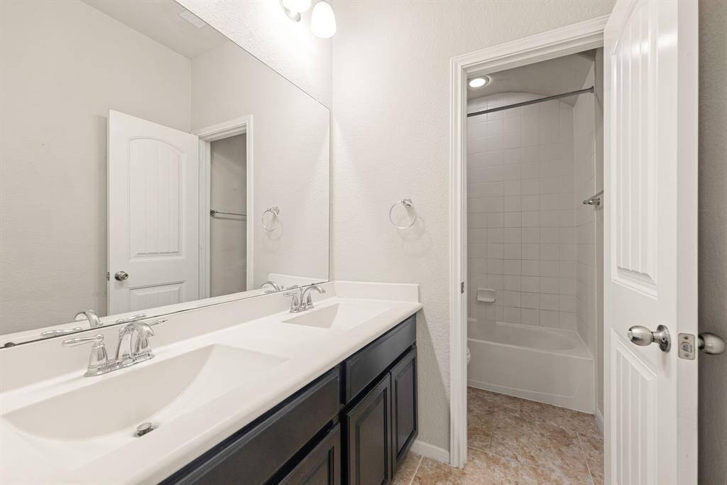 Secondary bath features tile flooring, bath/shower combo with tile surround, dark wood cabinets, beautiful light countertops, mirror, sleek fixtures and modern finishes.