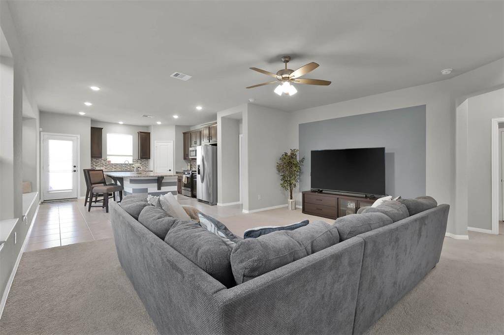 The room flows seamlessly into a modern kitchen with stainless steel appliances