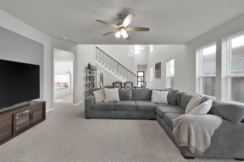 Natural light fills the room through multiple windows. A staircase leads to the upper level, and the space flows seamlessly into the additional bedroom downstairs