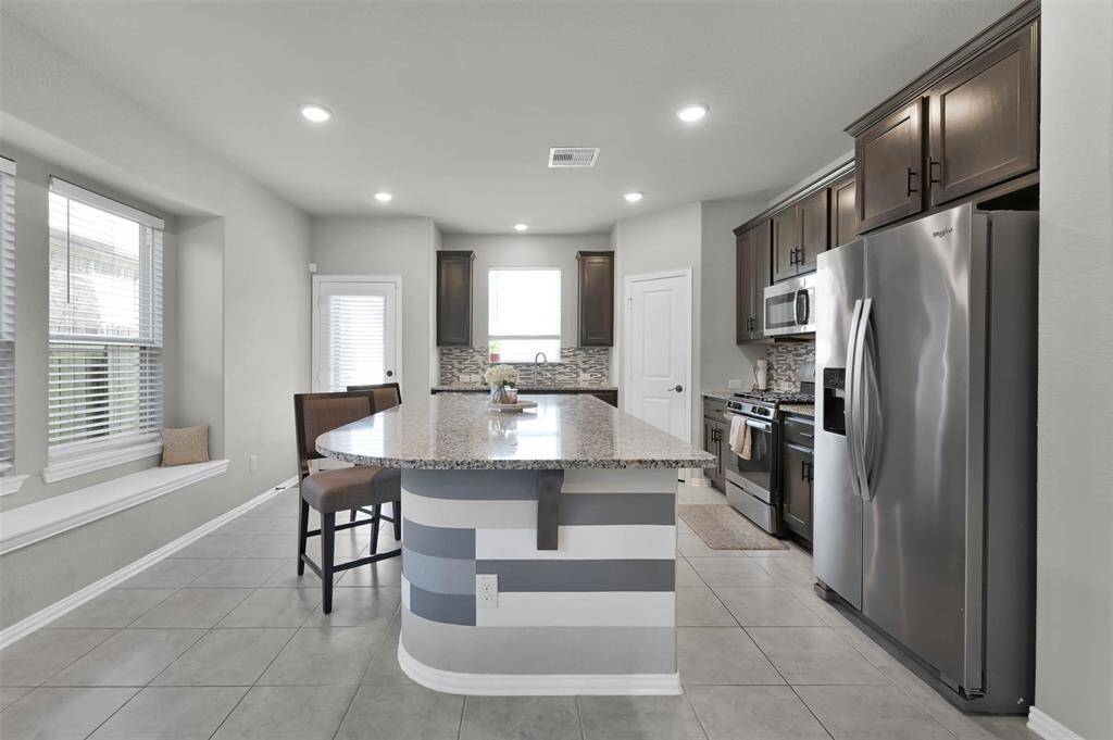This modern kitchen features a sleek design with dark wood cabinets, stainless steel appliances, and a large granite island for seating.