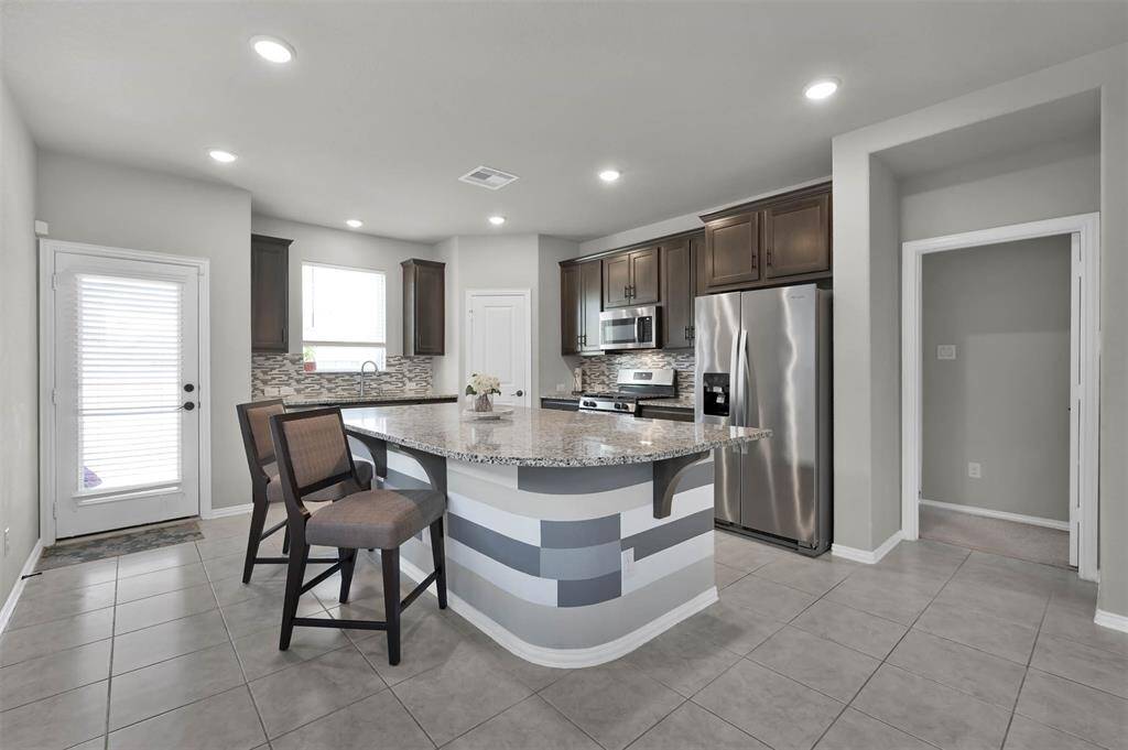 This kitchen features modern stainless steel appliances, dark wood cabinetry, and a stylish tile backsplash.