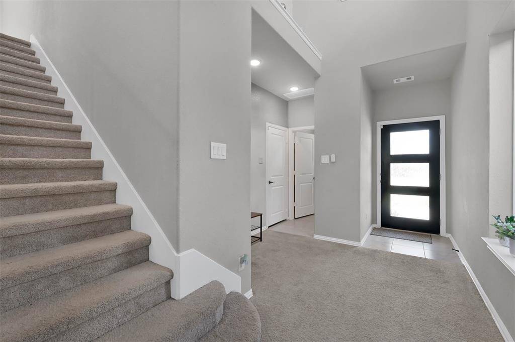 This photo showcases a modern entryway with a sleek front door featuring glass panels, MUD area off to the side leading to garage & separate laundry room