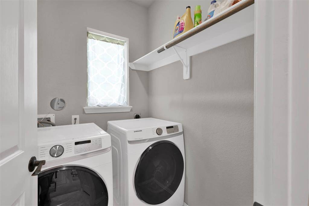 Compact laundry room just off the entryway features a small window for natural light & a white shelf above for storage