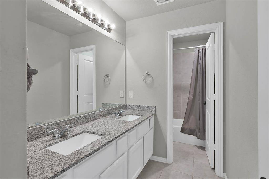 Upstairs full bathroom features a double-sink vanity with granite countertops & ample storage. It has a large mirror with overhead lighting and a separate area with a bathtub & shower
