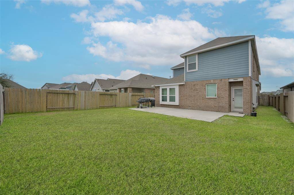 Spacious two-story home with a large fenced backyard, featuring a well-maintained lawn & a concrete patio area, perfect for outdoor activities & entertaining.