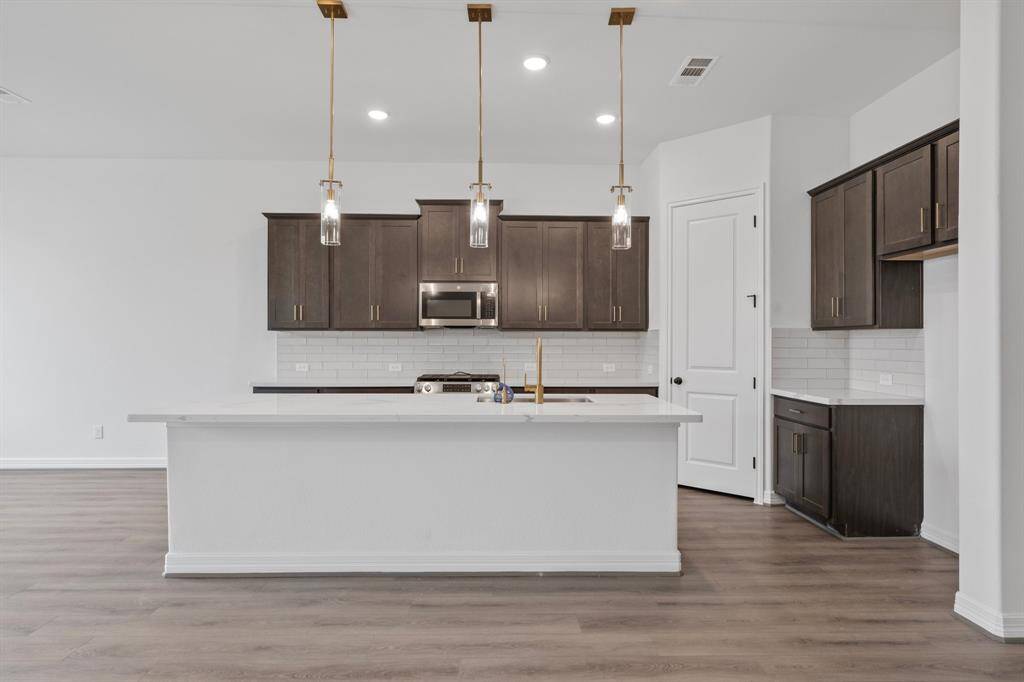 This light and bright kitchen features a large quartz island, dark stained cabinets, a large sink overlooking your family room, recessed lighting, and beautiful backsplash.
