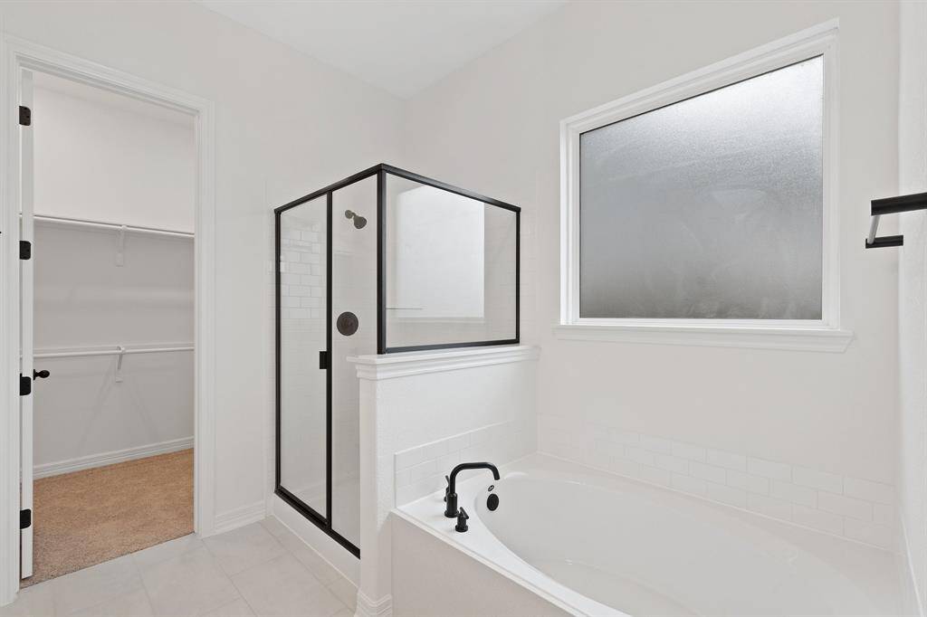 This additional view of your primary bathroom features tile flooring, fresh paint, walk-in shower, a separate garden tub, and a large walk-in closet.