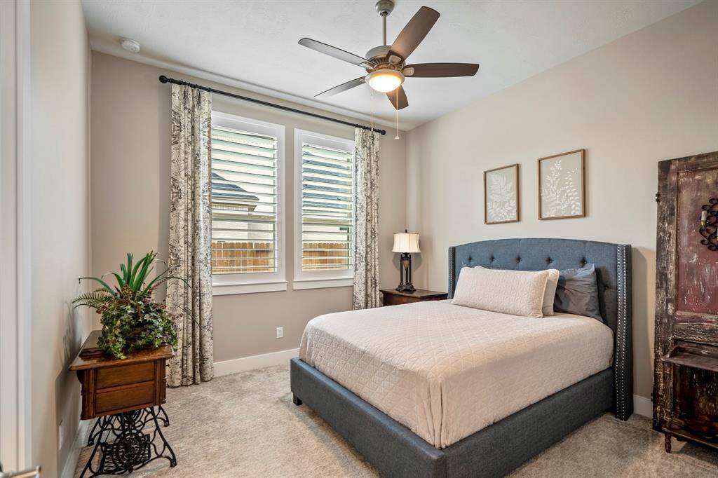 This spacious secondary bedroom features bright natural light, a ceiling fan, plush carpet, and custom window treatments!