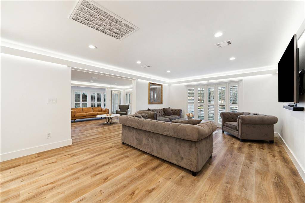 A spacious den provides additional room for gathering, featuring beautiful LVP flooring, ambient lighting, and soft neutral paint. A wall of windows with wood shutters frames stunning views, creating a bright and inviting space.