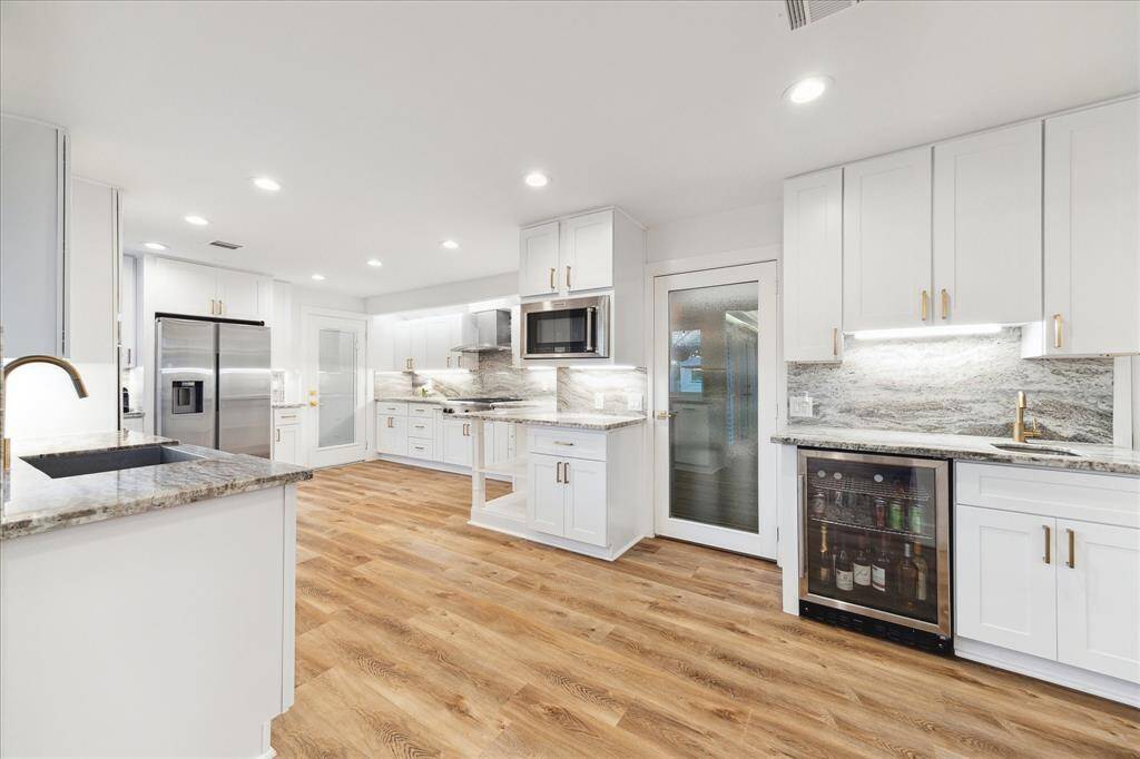 Show off your culinary skills in this exquisite kitchen, featuring marble countertops and backsplash, under-cabinet lighting, crisp white cabinetry with modern pulls, sleek stainless-steel appliances, a spacious walk-in pantry, and a wet bar with a second sink, beverage chiller, and additional storage.