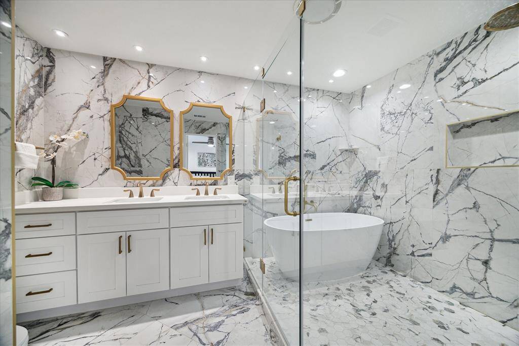 This luxurious ensuite bathroom will be your private retreat, wrapped in exquisite marble with chic lighting and modern finishes. Gold-tone fixtures and crisp white cabinetry add elegance, while a frameless glass enclosure showcases a stunning free-standing soaking tub and an incredible walk-in shower.