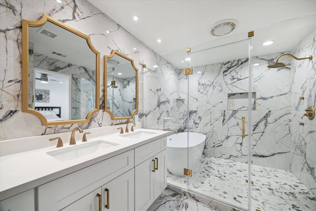 This spa-inspired ensuite offers a seamless blend of luxury and convenience. A frameless glass enclosure showcases exquisite marble, a free-standing soaking tub with wall-mounted fixtures and an oversized walk-in shower. Gold-tone fixtures and an upgraded shower head elevate the space, creating a refined and relaxing retreat.