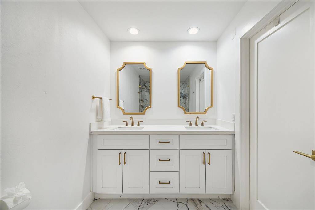 This immaculate ensuite bathroom features exquisite marble flooring, a dual sink vanity with oversized drawers for ample storage, and elegant gold-tone fixtures with coordinating mirrors. A separate water closet showcases a stunning oversized walk-in shower, creating a spa-like retreat.