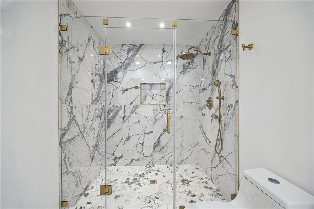 Enjoy the seamless beauty of frameless glass, striking marble, and premium gold-tone fixtures in this oversized walk-in shower, designed for both style and comfort.