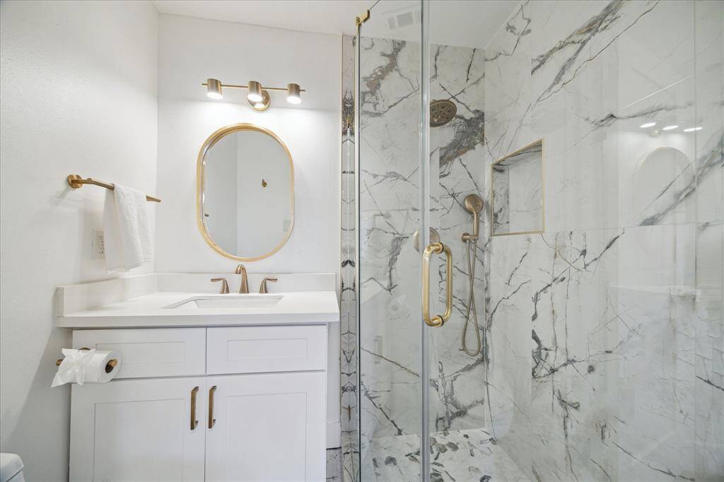 This stunning ensuite offers a single sink vanity with upgraded fixtures and a coordinating mirror above. The walk-in shower features elegant marble walls, a frameless glass enclosure, and upgraded gold-tone fixtures, creating a true spa-like retreat.