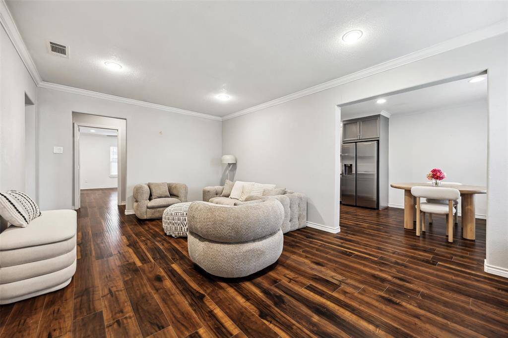The living area features warm flooring and opens into a dining space with a modern kitchen visible in the background, showcasing stainless steel appliances. The overall ambiance is cozy and inviting with a contemporary touch.