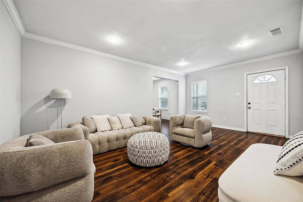 This welcoming living room features elegant floors and soft neutral walls. It’s well-lit with ample natural light from a window near the entrance, creating a warm, inviting atmosphere.
