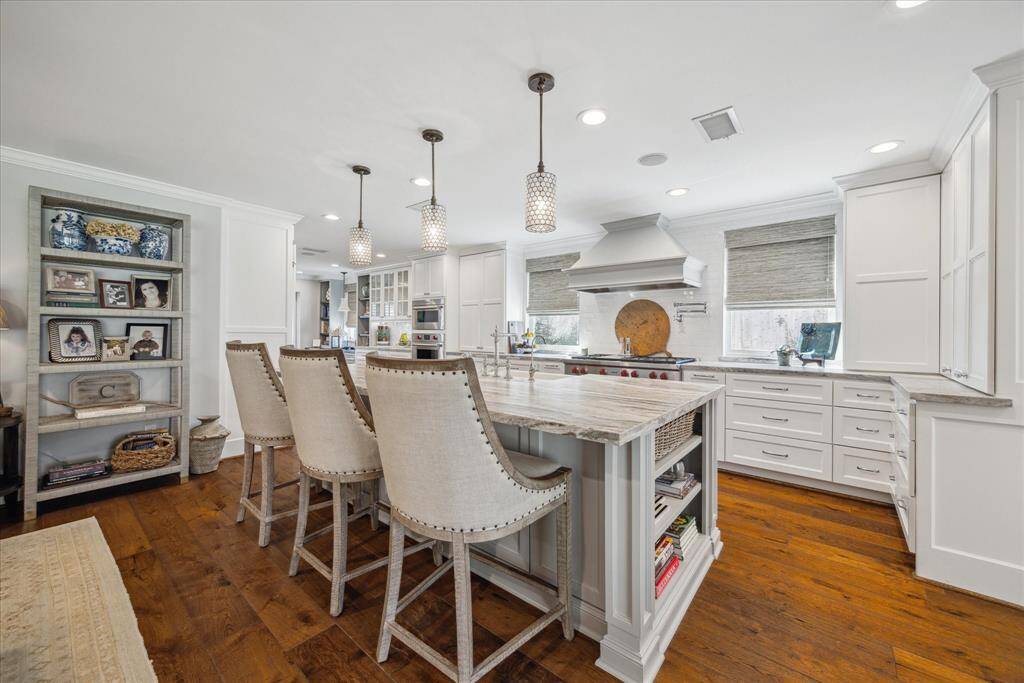 This photo showcases a bright, spacious kitchen with a large island complete with quartzite countertop. . A built-in shelf displays decorative items, adding a personal touch. The room is well-lit with pendant and recessed lighting.