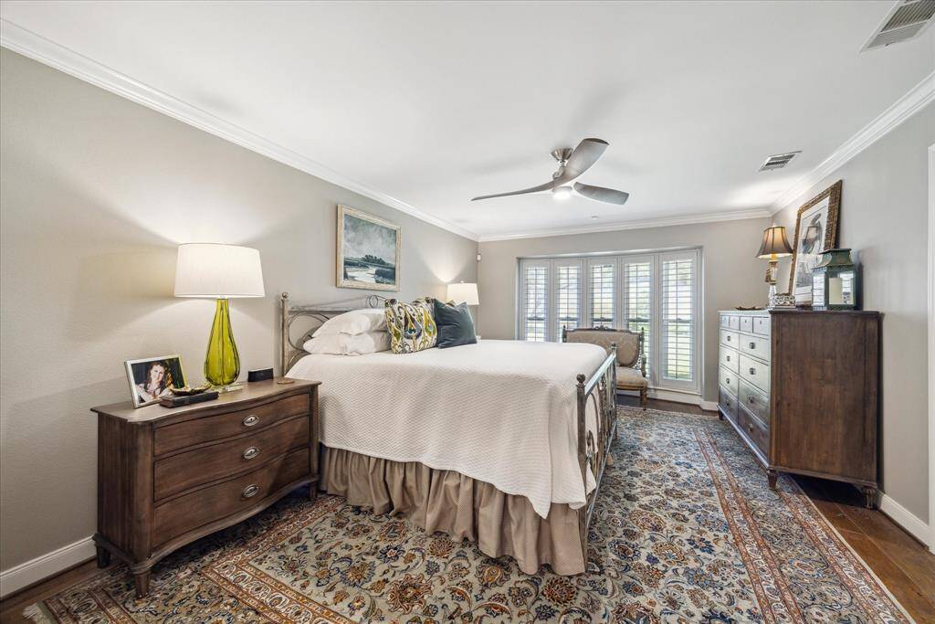 The primary bedroom features a spacious layout with a large window with shutters  allowing plenty of natural light and overlooking the backyard. The room is tastefully decorated, with a ceiling fan and a patterned area rug adding warmth and style.