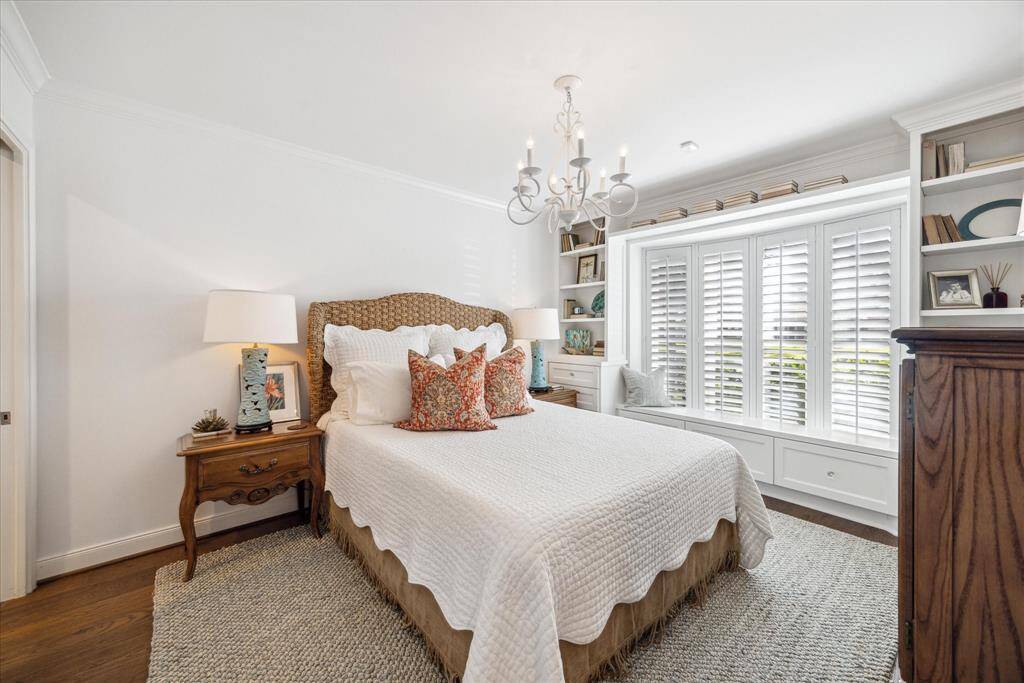 This cozy bedroom features a stylish chandelier, and ample natural light from large windows with shutters. Built-in shelves enhance storage .