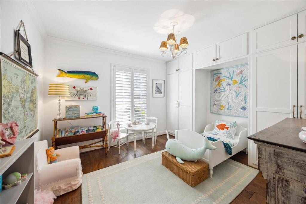 Bright and charming children's room with wooden floors, built-in storage, and playful decor. Features a cozy seating area, book display, and large windows with shutters allowing natural light. Ideal for a family-friendly home.