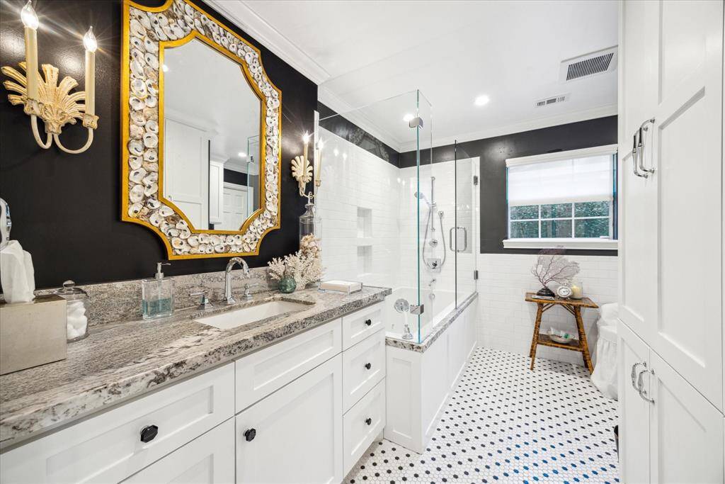 This downstairs bathroom features a modern design with elegant black and white decor. It includes a granite countertop with a single sink and stylish lighting fixtures. The shower is enclosed with glass, and there's a window providing natural light. The floor has a classic black and white tile pattern.