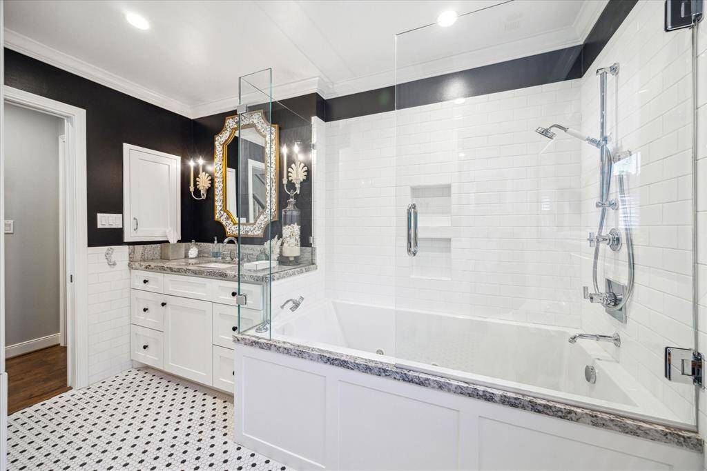 This bathroom features a sleek, modern design with a glass-enclosed bathtub and shower, elegant black and white color scheme, and stylish fixtures. Marble countertops enhance the luxurious feel, complemented by classic white subway tiles and patterned floor tiles.