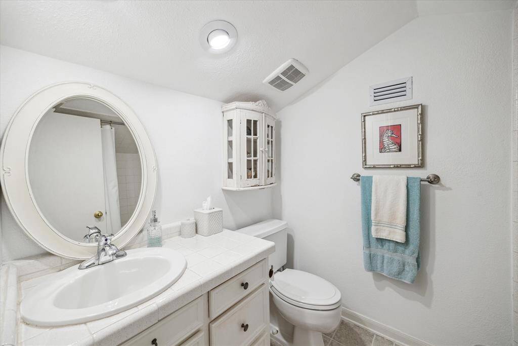 This upstairs  bathroom features a clean, white design with a round mirror above a tiled vanity. It includes a toilet, tub/shower , a mounted towel rack, and a small cabinet for storage, creating a bright and functional space.