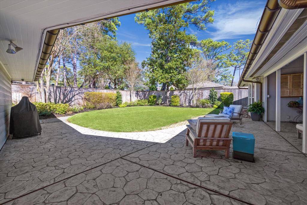This photo showcases a spacious backyard with a well-maintained lawn and a large patio area. The patio features comfortable seating and a covered section, ideal for outdoor relaxation and entertaining. The yard is enclosed by a wooden fence, providing privacy .