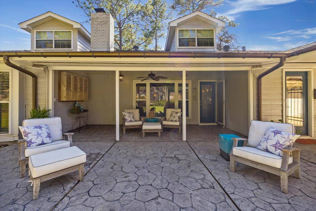 This photo showcases a charming outdoor patio area with comfortable seating and a rustic finish. The space is partially covered, providing shade and features a ceiling fan for added comfort. It's an inviting spot for relaxation or entertaining guests.