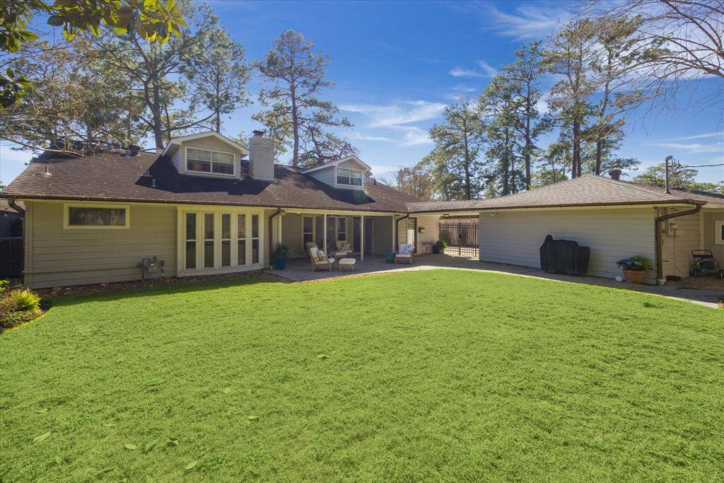 This photo showcases a charming home with a spacious, well-maintained backyard. The house features a covered patio area, perfect for outdoor relaxation, and large windows that allow plenty of natural light. Surrounded by mature trees, it offers a serene and private setting.