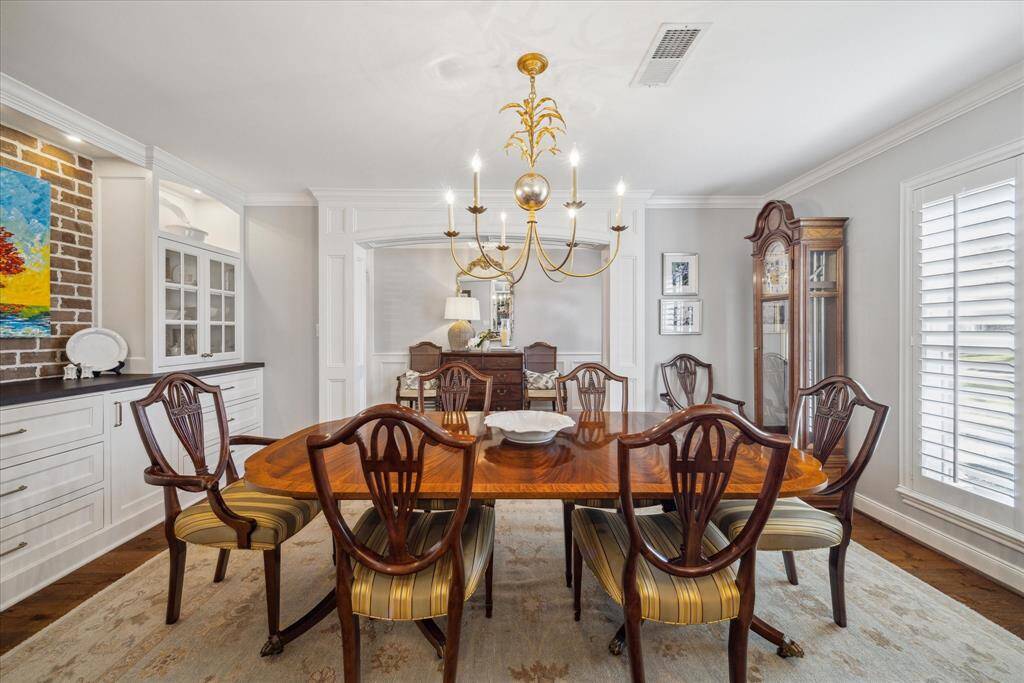 This elegant dining room features a   a stylish chandelier and is accented by a brick feature wall, built-in cabinetry, and tasteful decor, creating a warm and inviting space.