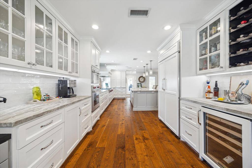 The kitchen features elegant white cabinetry with glass fronts, a spacious layout, and wood floors. It includes modern appliances, Wolf oven and Microwave/ covection oven ,wine fridge and ample counter space, creating a bright and functional cooking area.