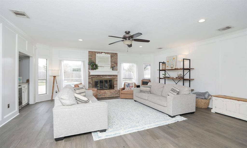 This spacious living room features a cozy brick fireplace, large windows, and a ceiling fan.