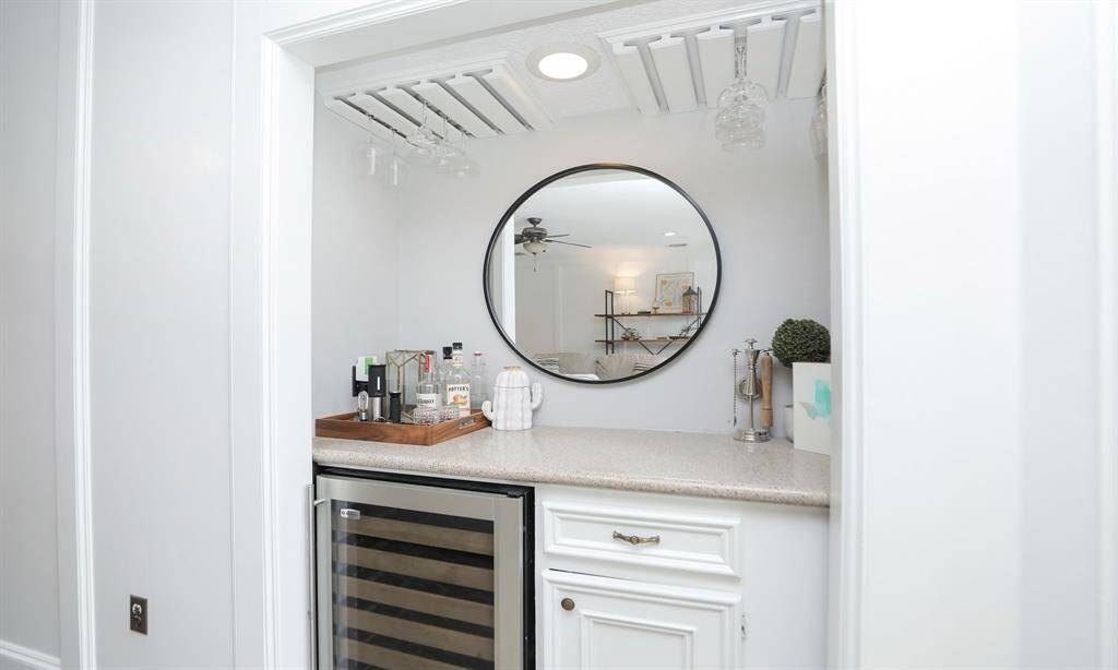 A stylish dry bar nook with a sleek wine cooler, granite countertop, and hanging glassware rack.